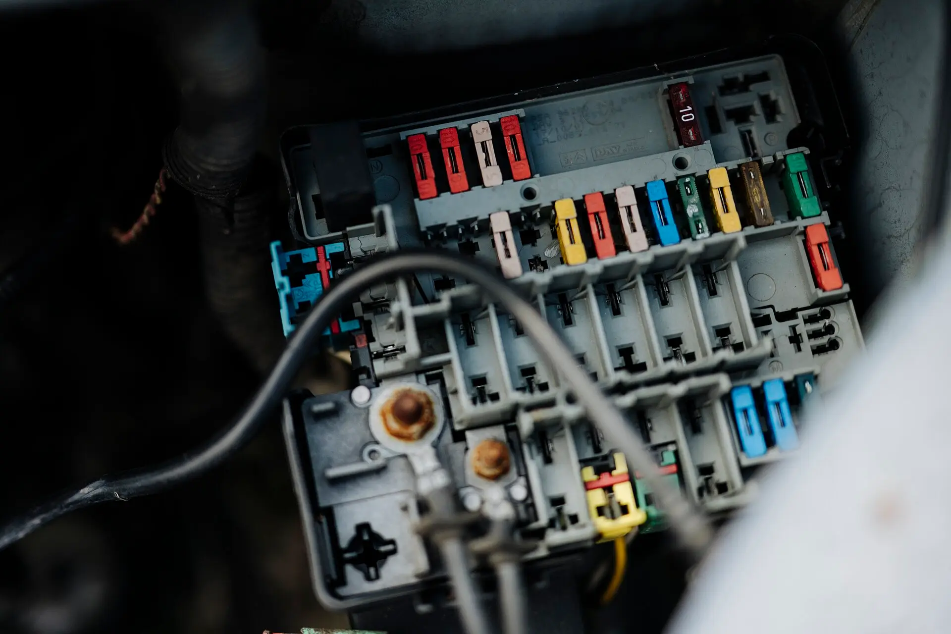 A car fuse box with its cover removed showing coloured fuses