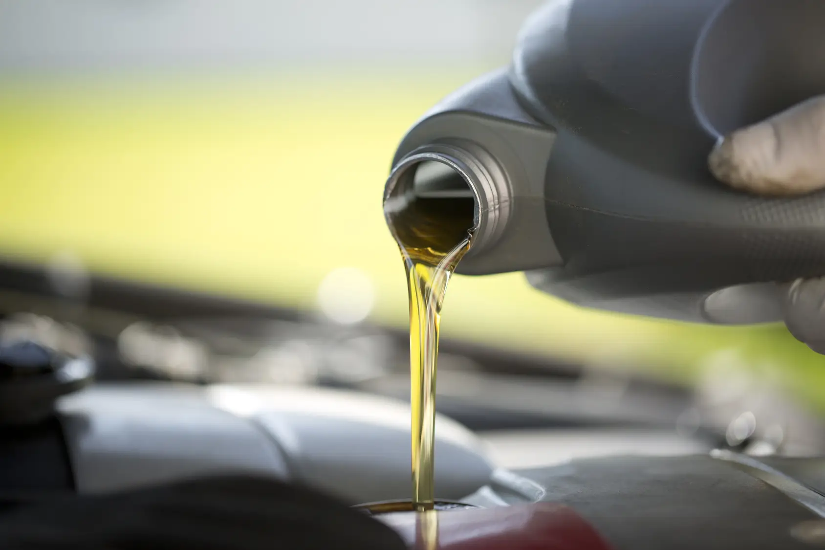 Fresh engine oil pours from a bottle into an engine